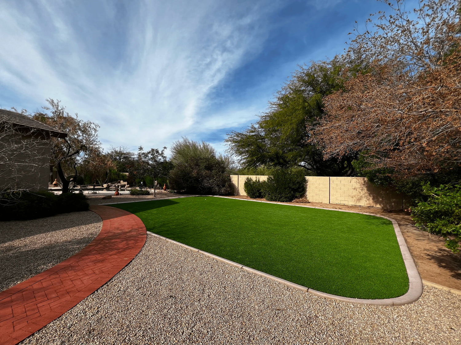 Artificial grass installation in a residential backyard with trees and a clear sky.
