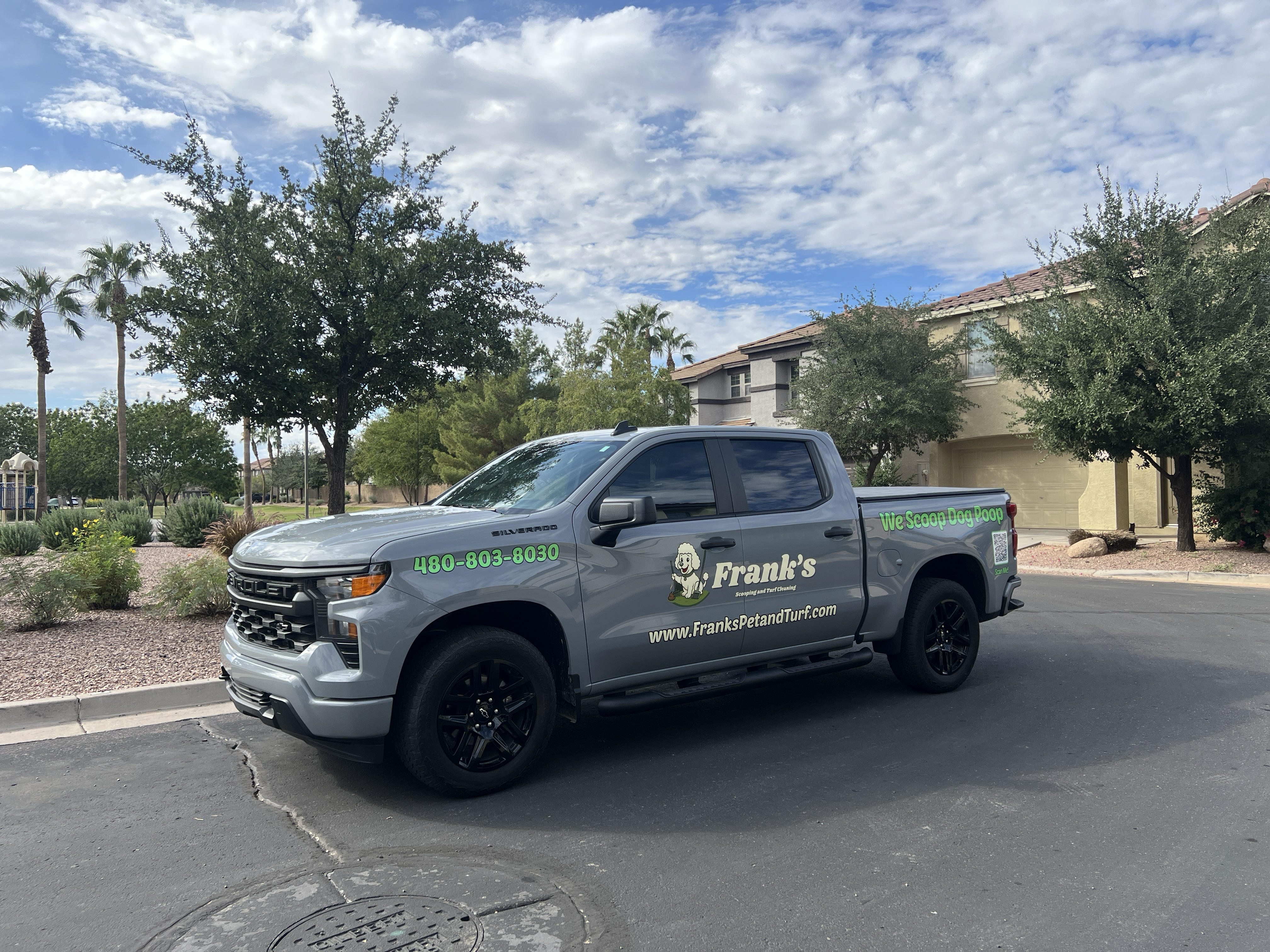Gray truck with branding on a street with trees and buildings in the background