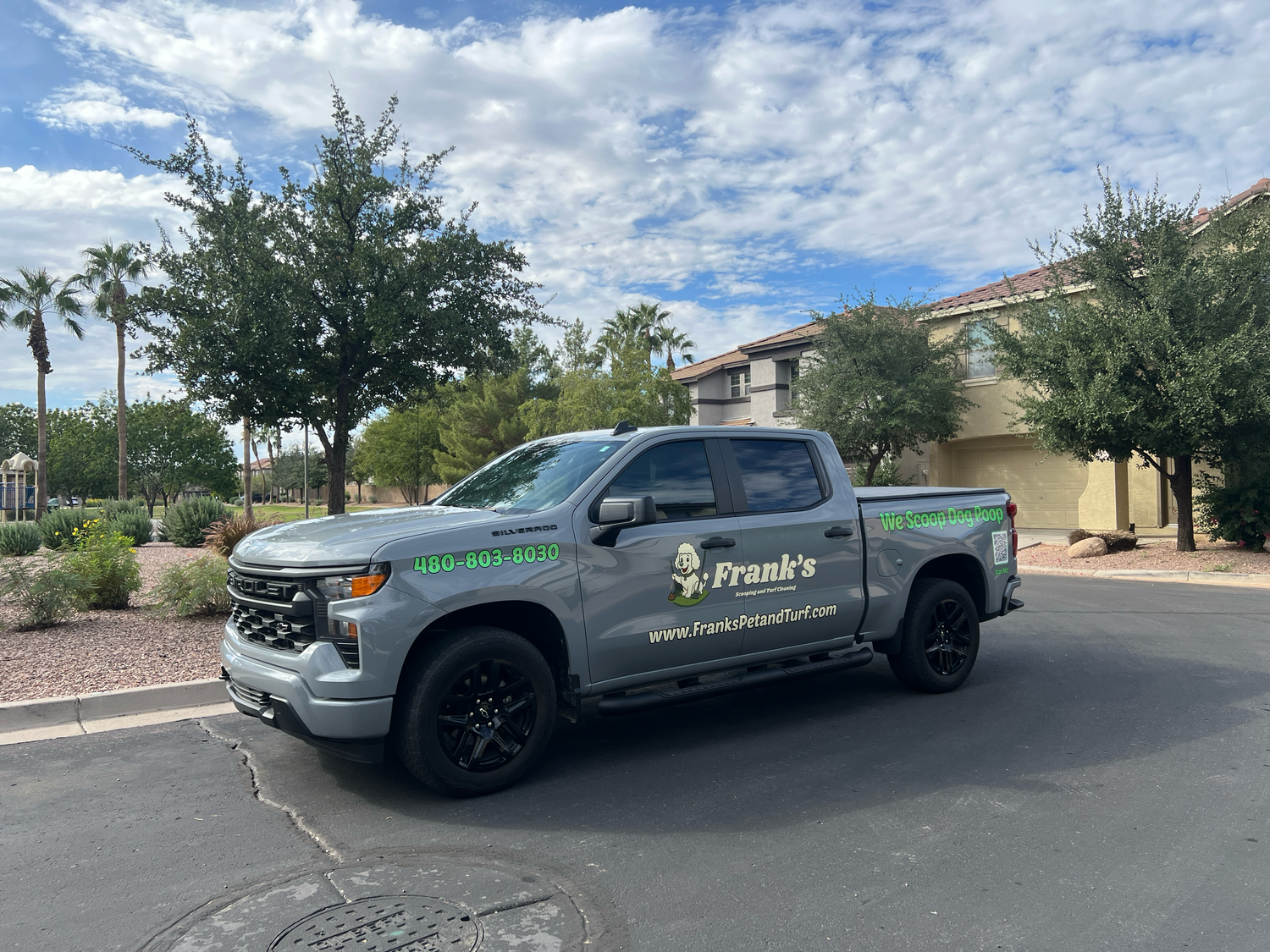 Gray truck with branding on a street with trees and buildings in the background
