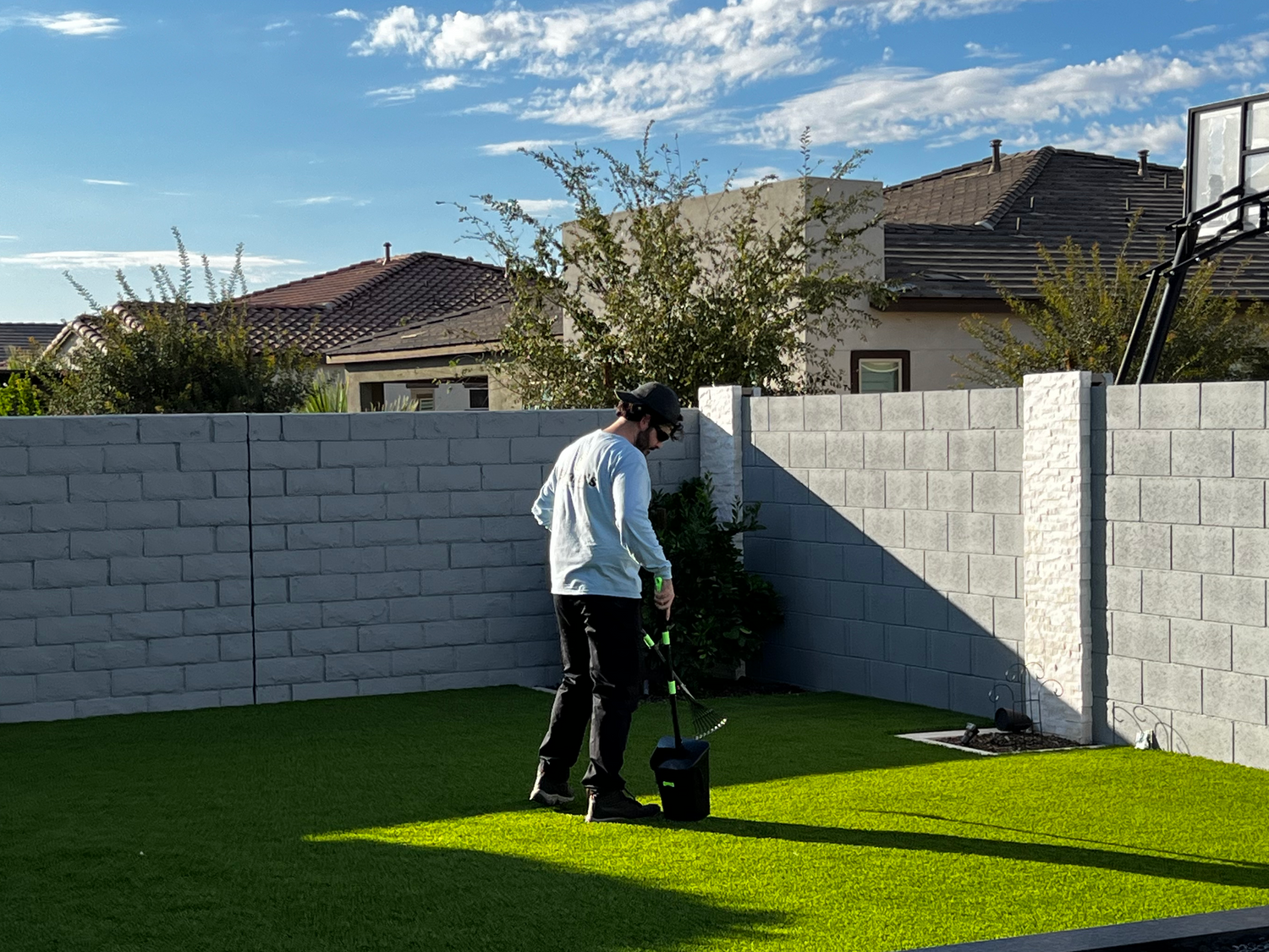Person cleaning a basketball hoop in a backyard with a clear sky