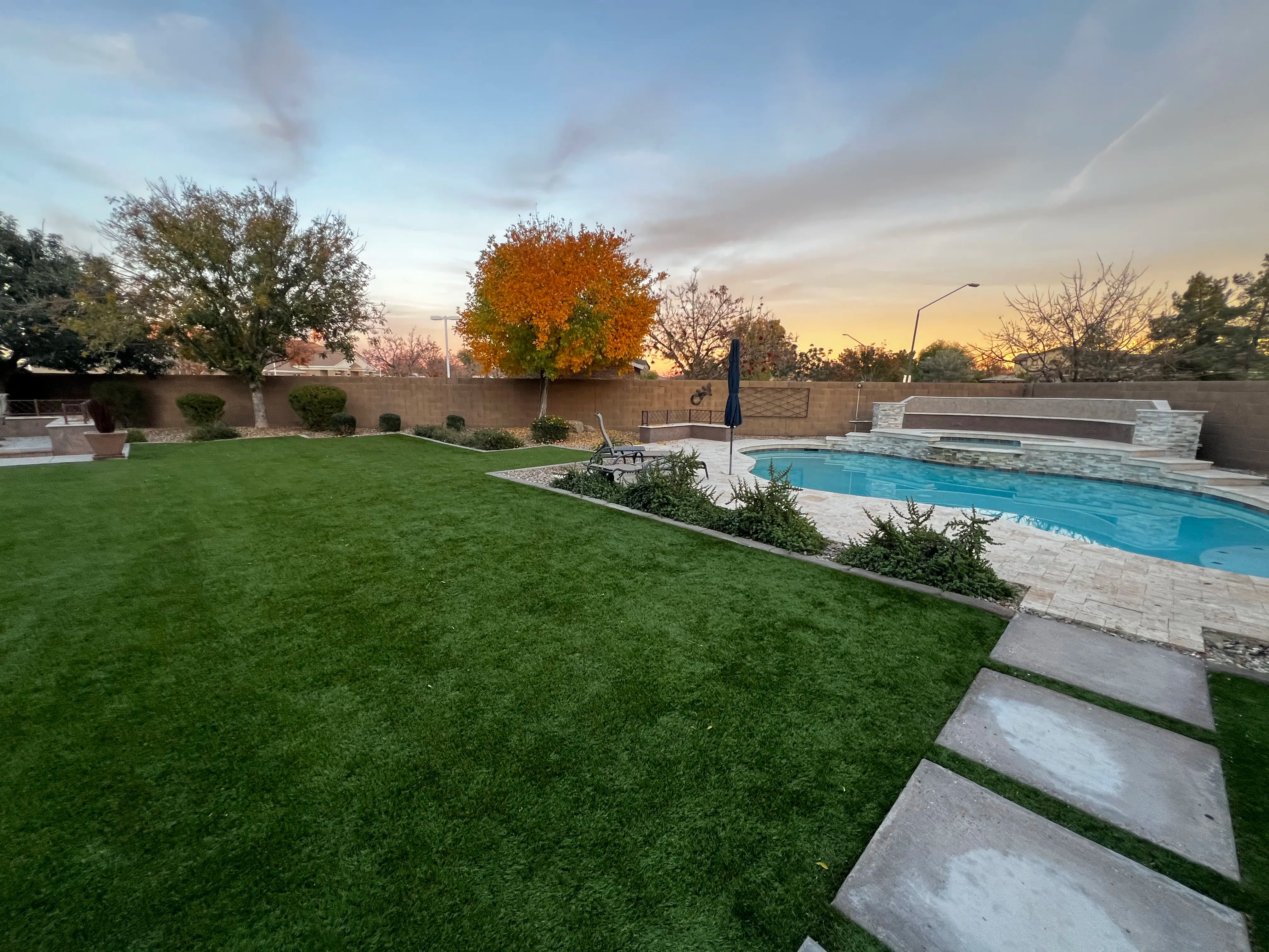 Backyard with pool, grass, and trees during sunset.