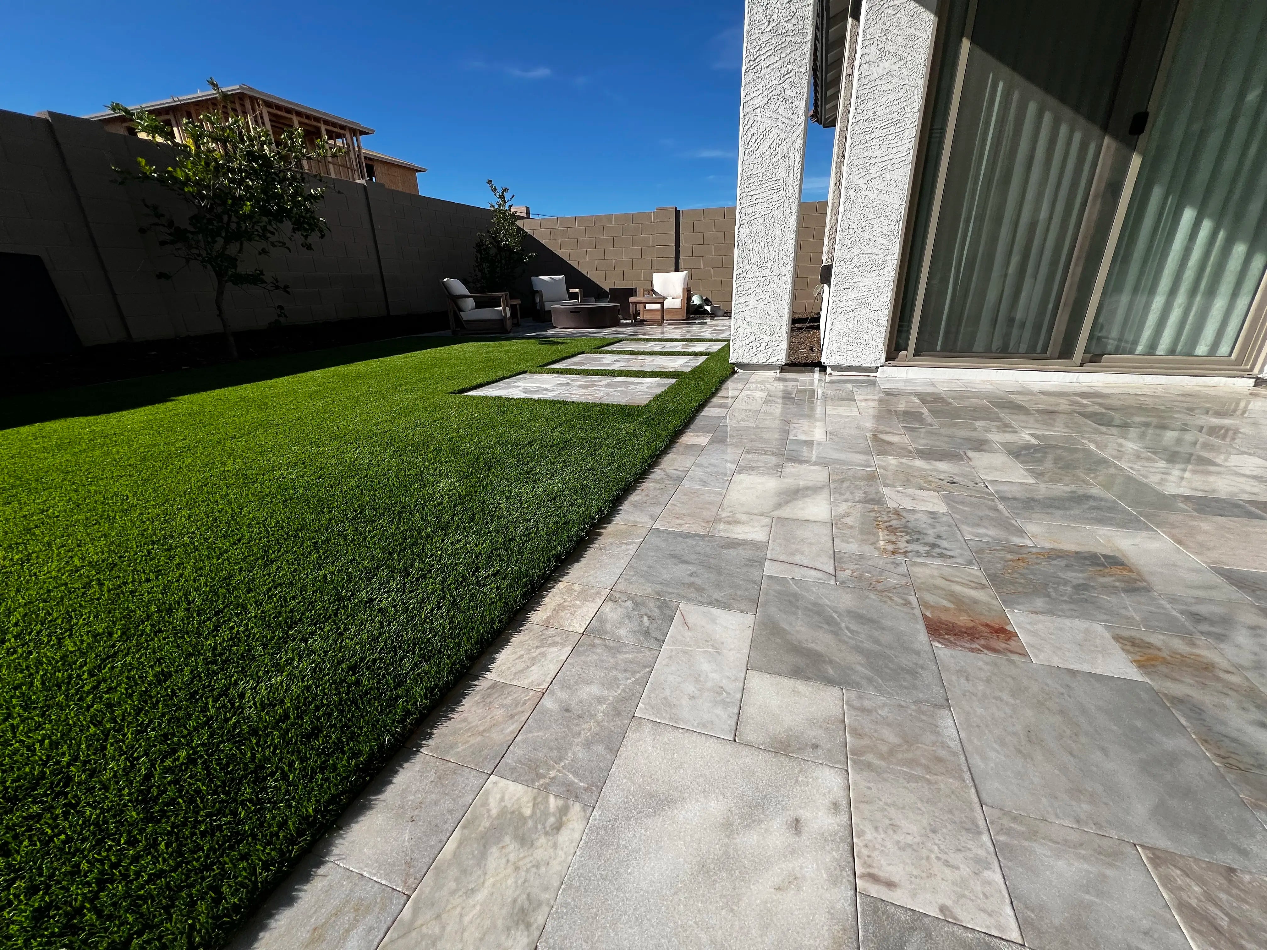 Close up of clean travertine and artificial grass with a sliding door and patio furniture in the background.