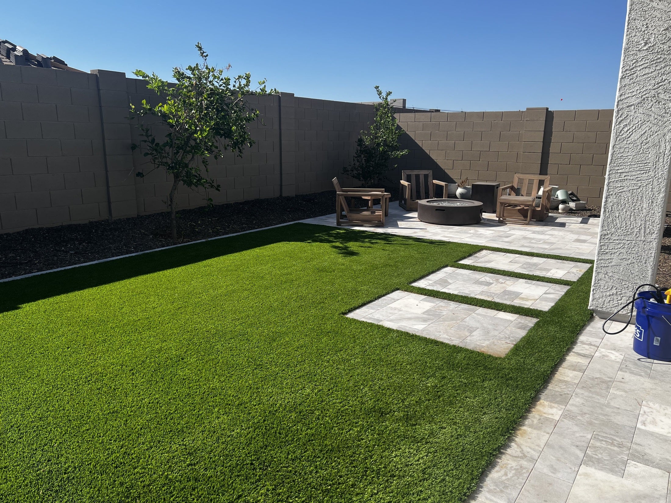 Backyard with artificial grass, patio stones, and outdoor furniture under a clear blue sky.