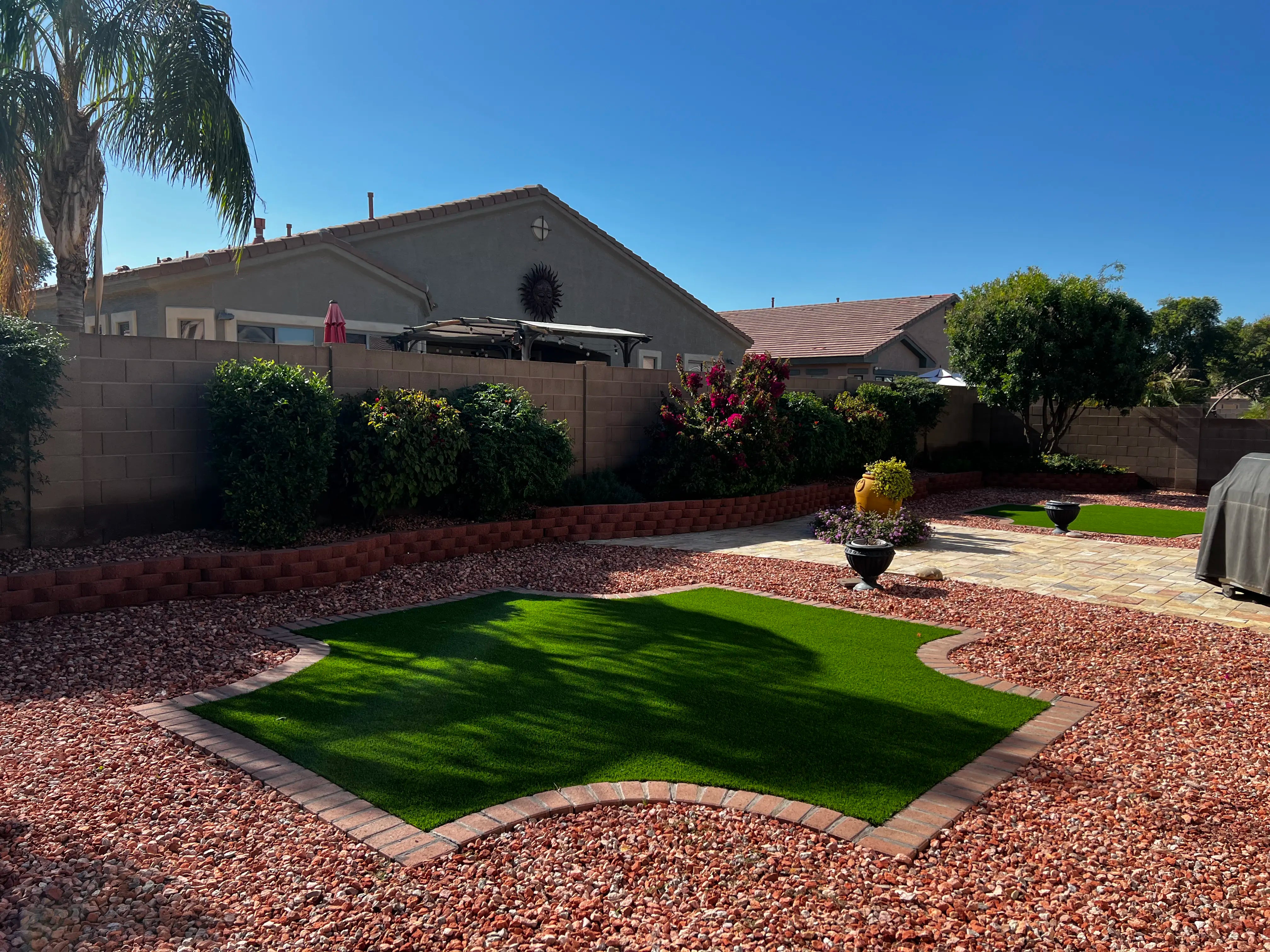 Backyard with artificial grass, pavers, and a house in the background